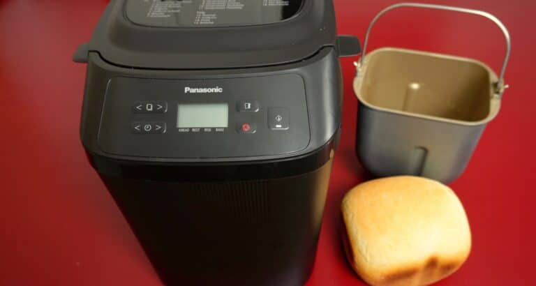 Panasonic mini brotbackautomat PN100 in schwarz mit Brot und Backform auf rotem Tisch